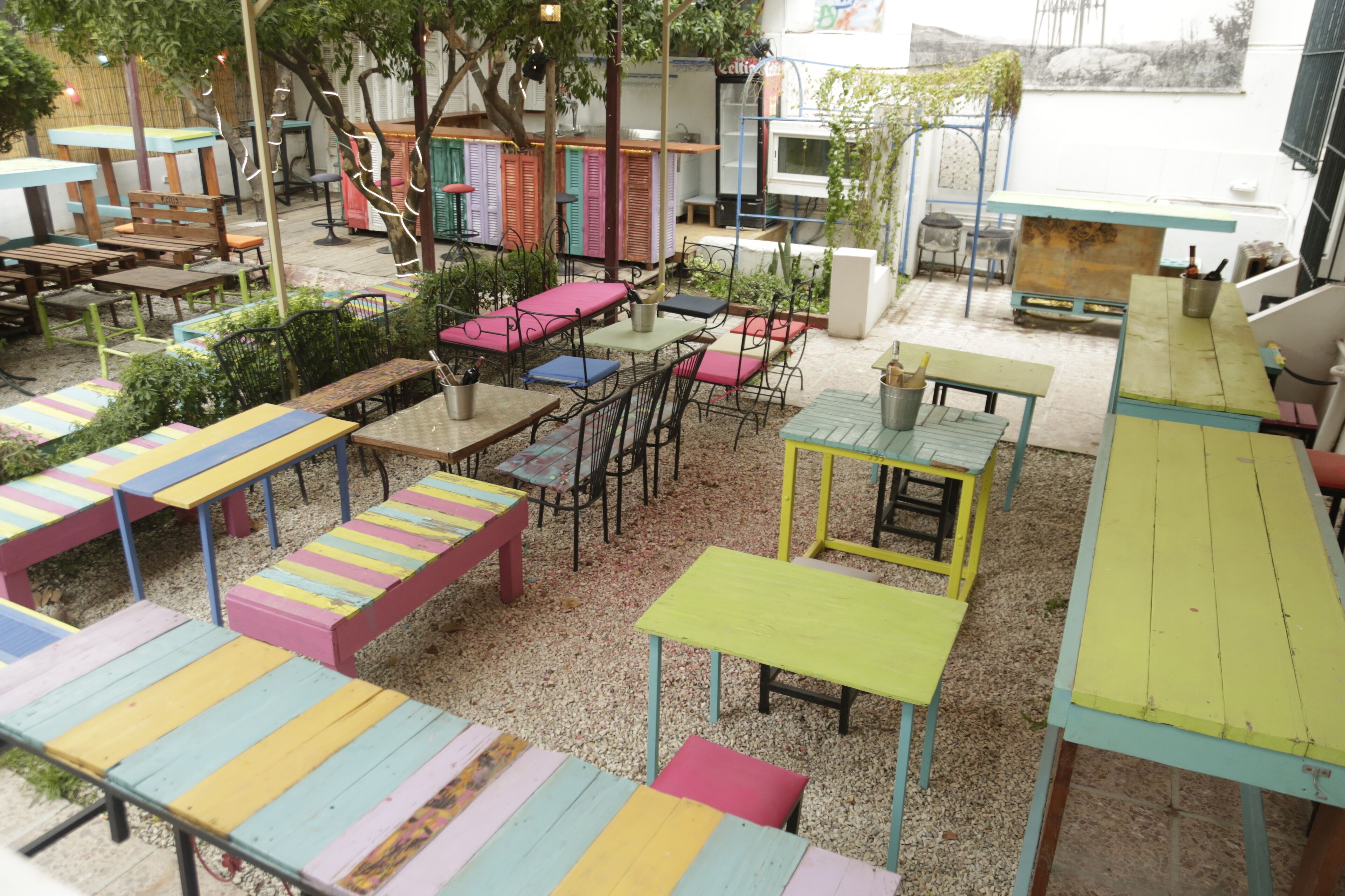 Un patio al aire libre con varias mesas y sillas, algunas con cojines coloridos a rayas.