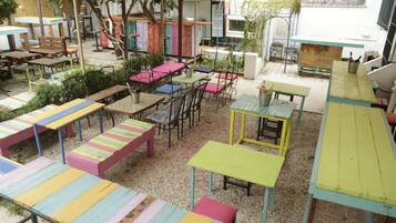 Un patio al aire libre con varias mesas y sillas, algunas con cojines coloridos a rayas.
