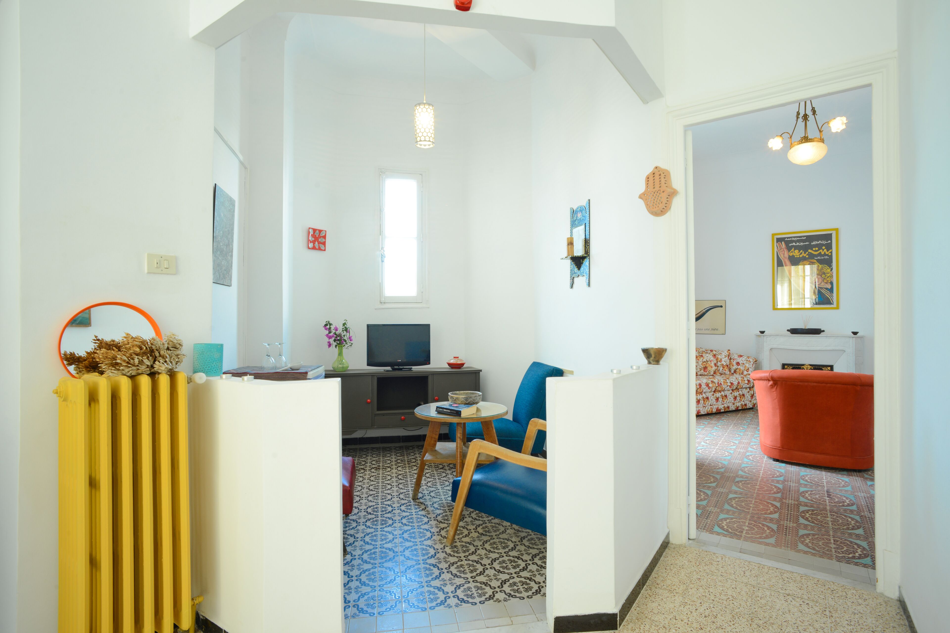 Una sala de estar con televisor, sofá y mesa de centro. Se observa un radiador y una ventana.
