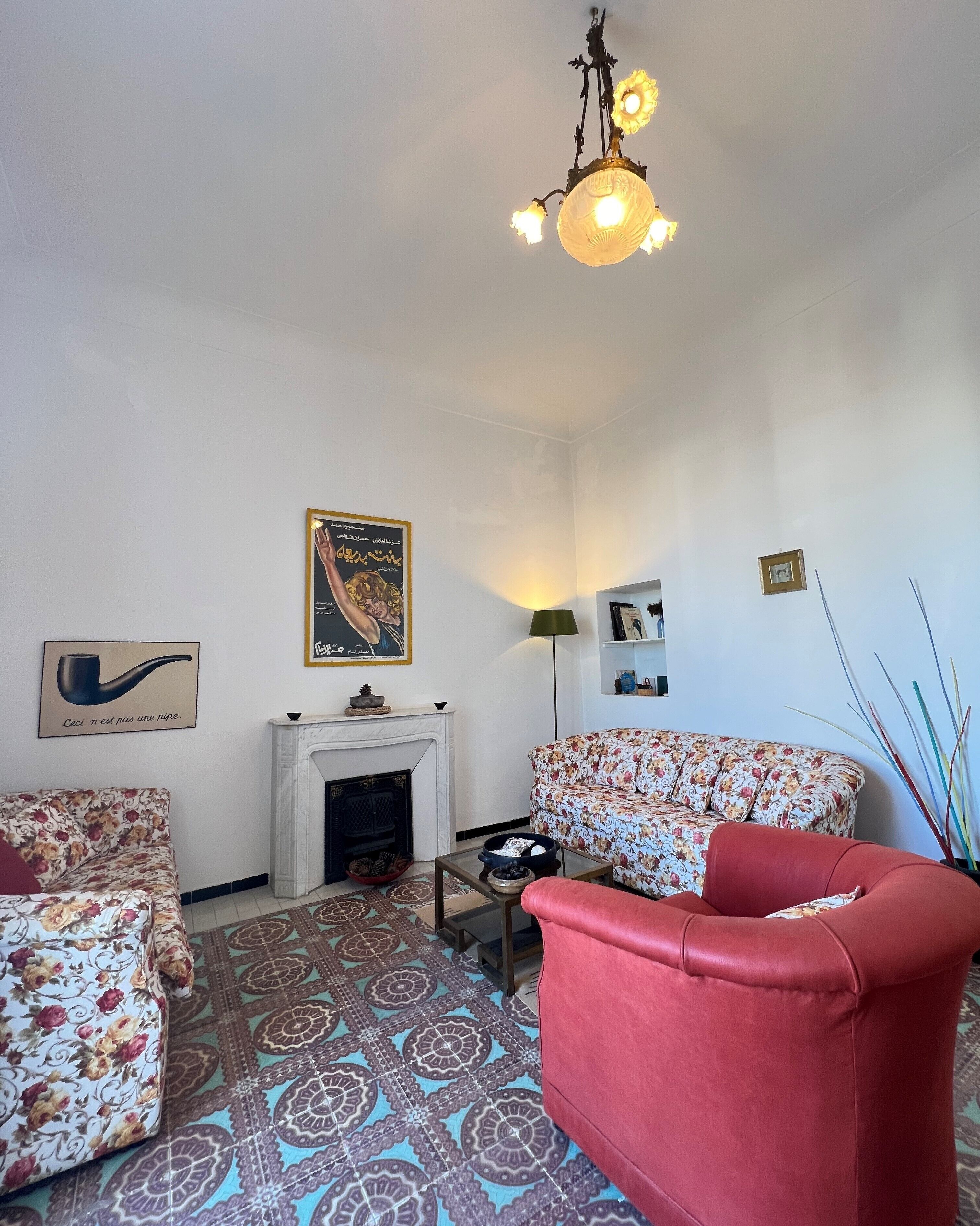 Sala de estar com lareira, sofás com padrão floral, uma poltrona vermelha e um lustre.