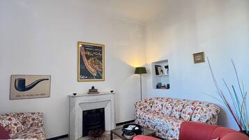 A living room with a fireplace, floral-patterned sofas, a red armchair, and a hanging light fixture.