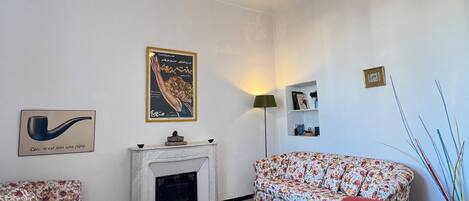 Un salon doté d’une cheminée, de canapés à motifs floraux, d’un fauteuil rouge et d’un luminaire suspendu.