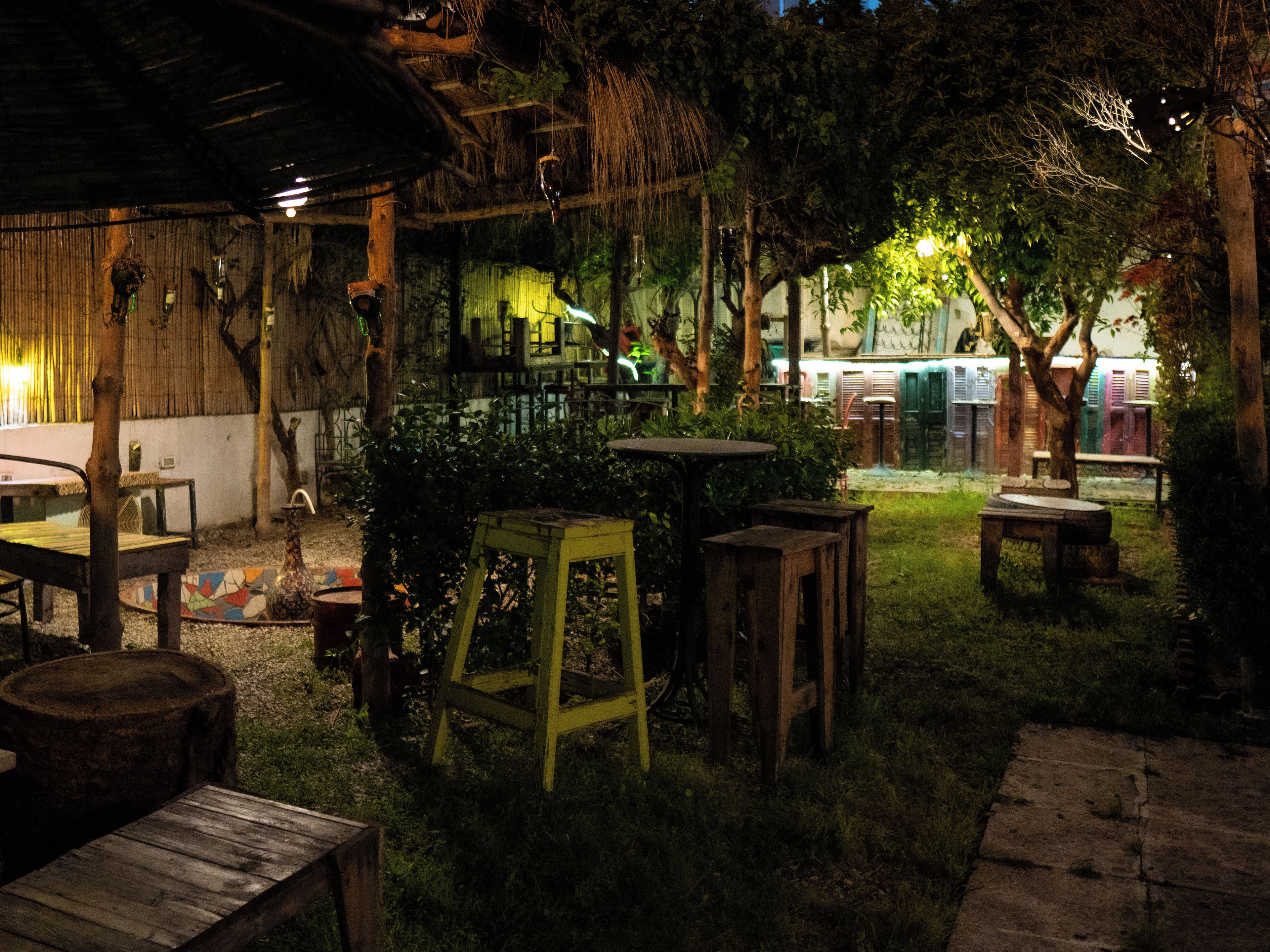 An outdoor seating area with tables and chairs, surrounded by greenery and trees.