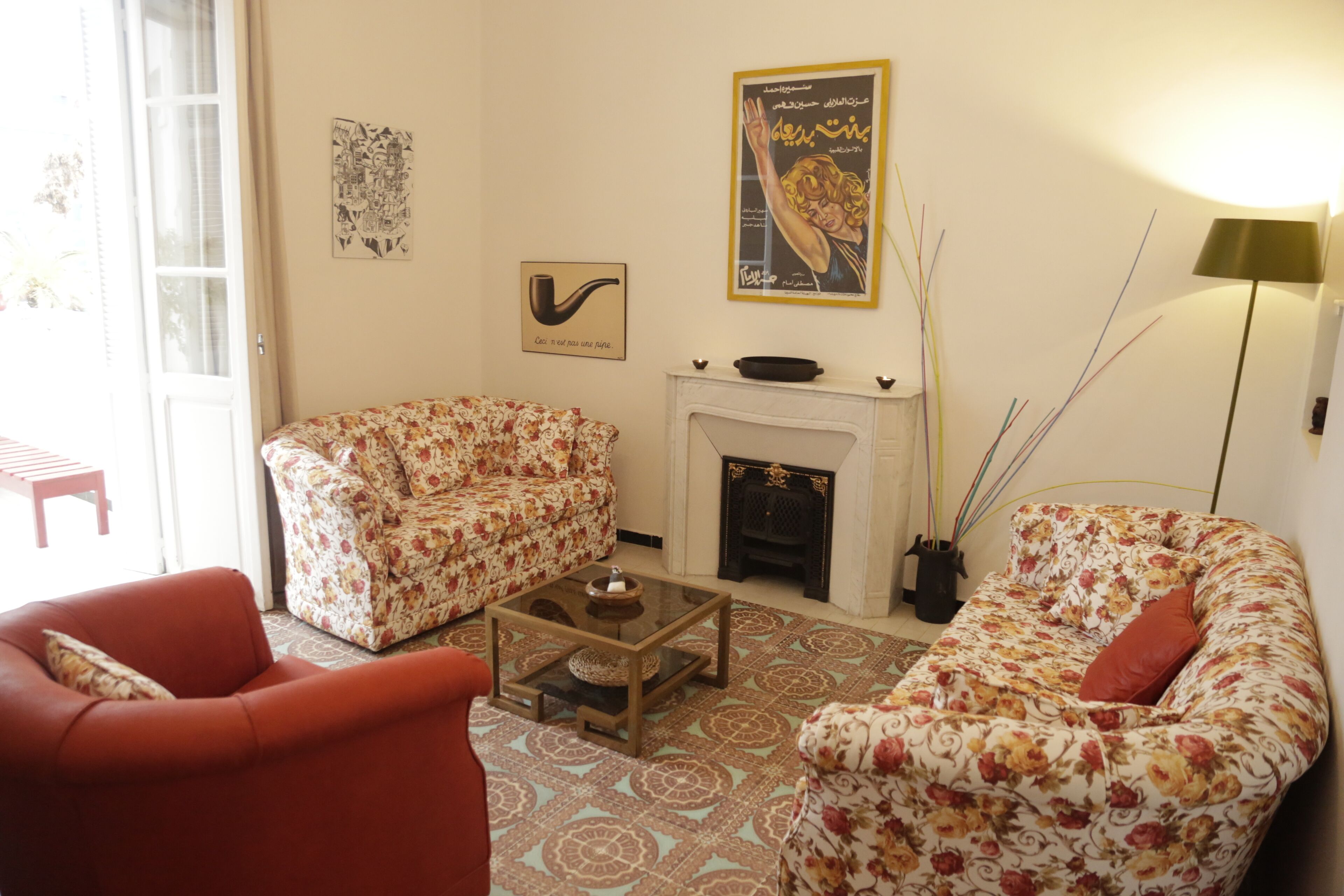 Sala de estar con sofás de estampado floral, una mesa de centro de vidrio, chimenea y cuadros en la pared.