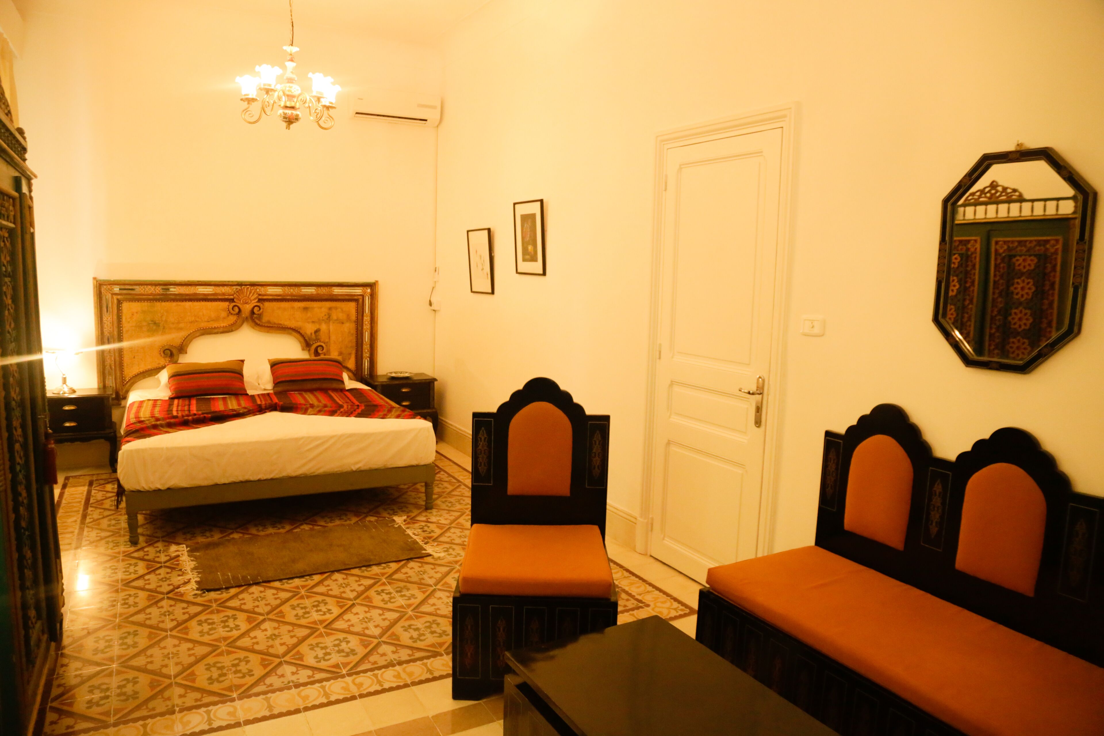 Une chambre à coucher avec un lit, deux tables de chevet, un banc, un lustre et une porte.