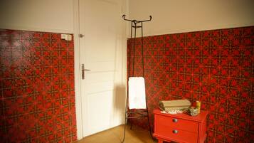 A room with patterned red and black tiles, a white door, a red dresser with drawers, and a metal drying rack with a white towel.
