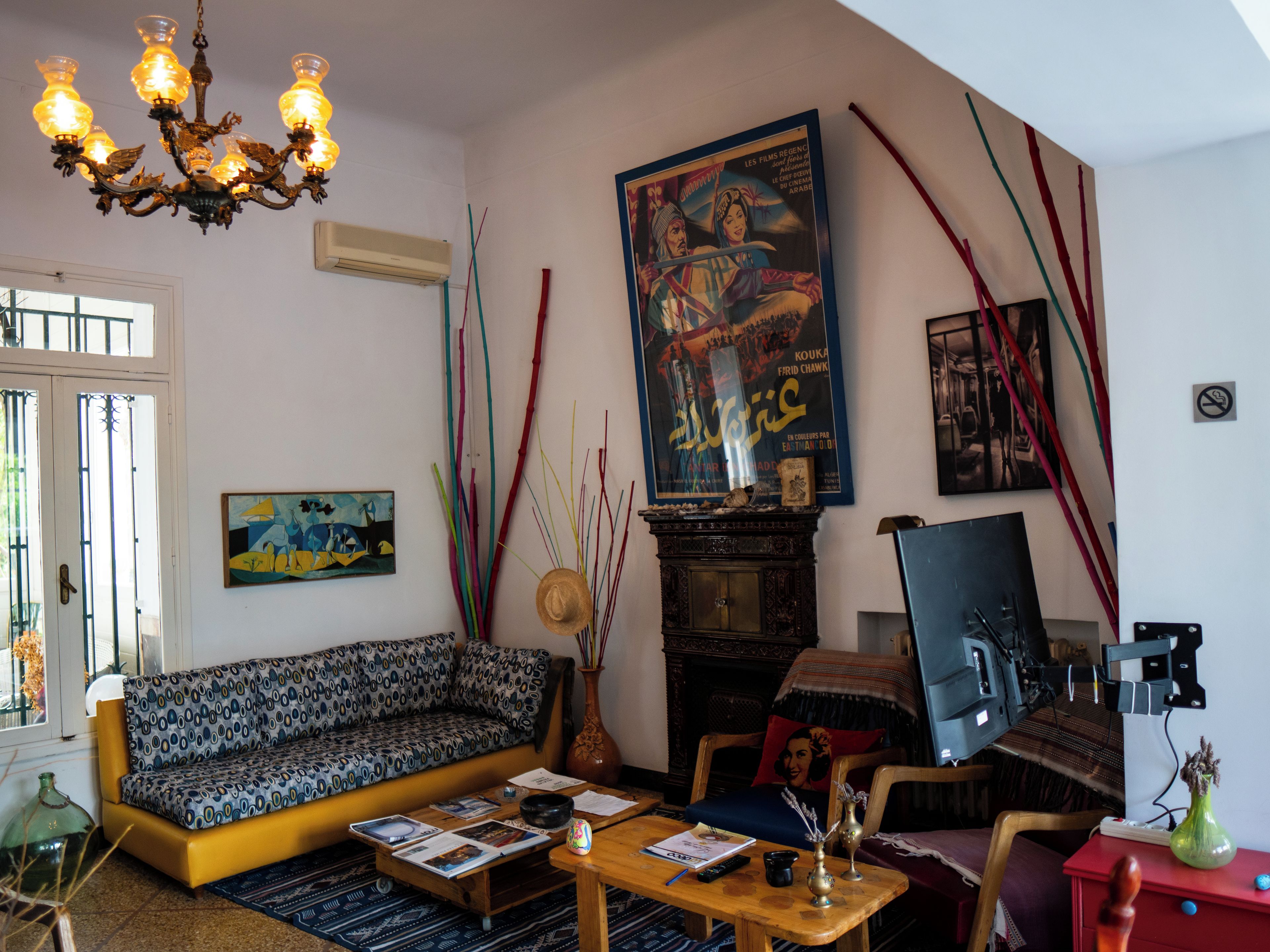 Un salon avec un canapé à motifs, une table basse sur laquelle sont posés des livres, une cheminée et une grande affiche accrochée au mur.