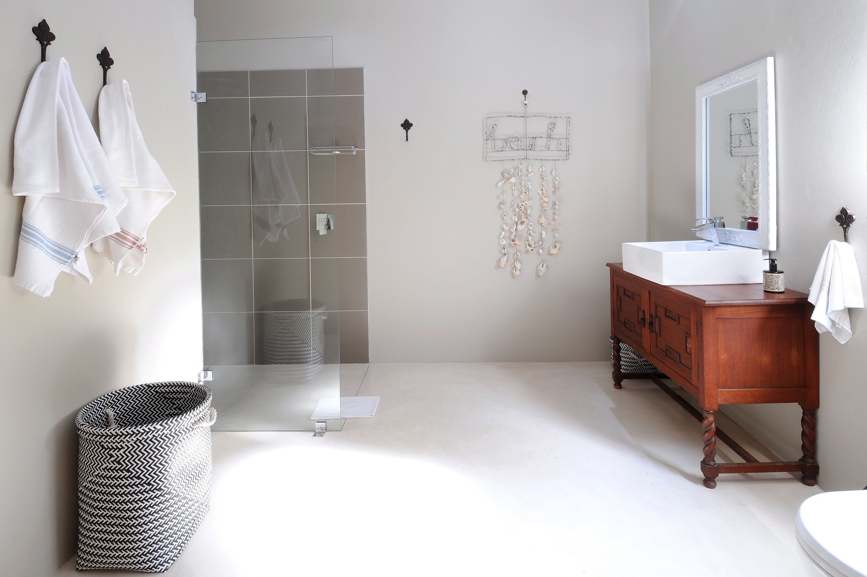 Un baño con cabina de ducha de vidrio, tocador de madera con espejo y un perchero para toallas.