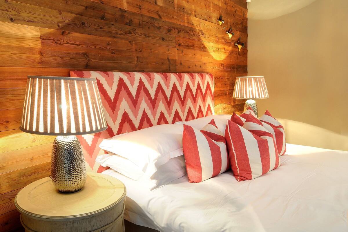 A bed with striped pillows and a lamp on a wooden floor.