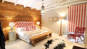 A bedroom with a wooden headboard, a bed with white bedding, a bench, a red chair, and a cowhide rug. - Ocean Breeze (Kenton on Sea)