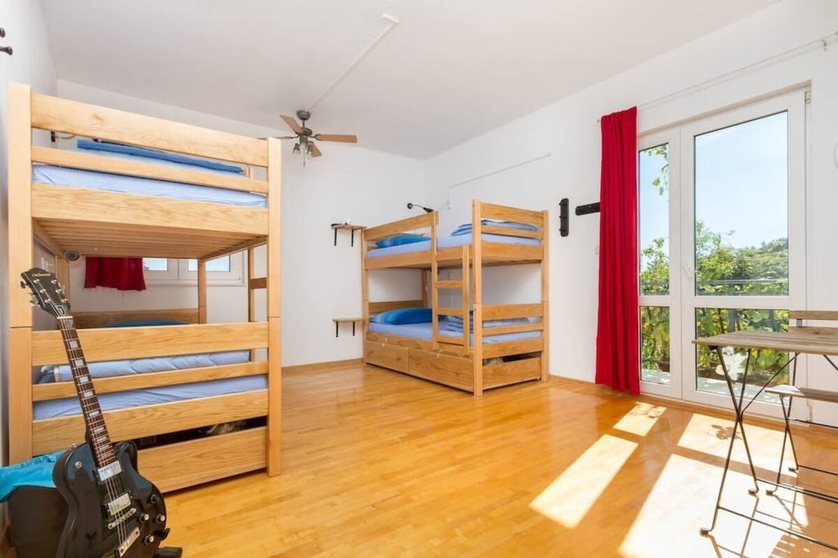 A room with two bunk beds, a ceiling fan, a window with red curtains, and a guitar on the floor.
