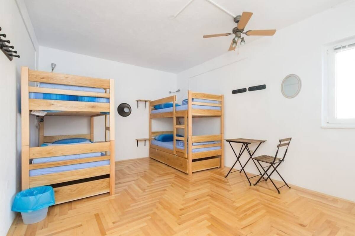 A room with two bunk beds, a ceiling fan, a small table with chairs, and a window.