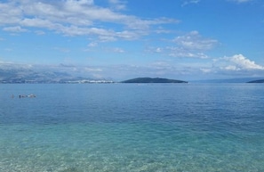 A clear view of a calm sea with a distant island and a few people swimming. - Hostel Oktarin (Kastela)