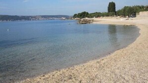 Una playa con agua cristalina, orilla pedregosa y árboles a lo lejos.