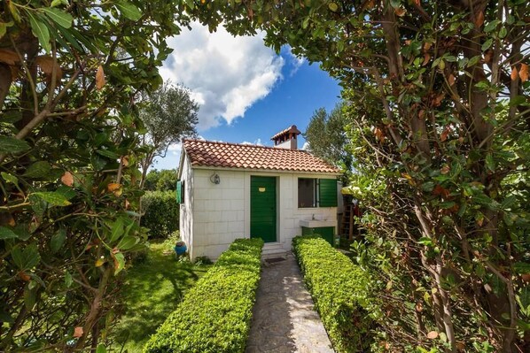 Un pequeño edificio con techo de tejas, una puerta verde y un sendero que conduce a él.