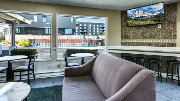 A modern interior with a sofa, dining table, and chairs. A TV is mounted on the wall, and there is a view of buildings outside.