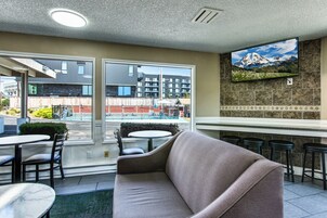 Un interior moderno con un sofá, una mesa de comedor y sillas. Un televisor está montado en la pared, y se ve una vista de edificios desde el exterior.