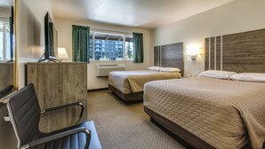 A hotel room with two beds, a desk, a chair, a window with curtains, a wall-mounted TV, and a lamp.