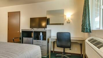 A hotel room with a bed, a desk, a chair, a dresser, a mirror, a heater, and a window with curtains.