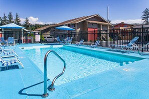 A swimming pool with lounge chairs and umbrellas, surrounded by a fence and buildings.
