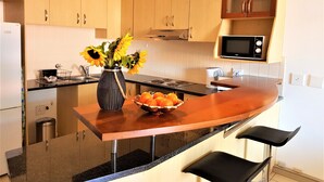A modern kitchen with wooden cabinets, a black microwave, a sink, and a vase with sunflowers on the counter. - 12 Simonsplein (Stellenbosch)