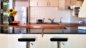 A modern kitchen with wooden cabinets, a stainless steel refrigerator, a sink, and two bar stools. - 12 Simonsplein (Stellenbosch)