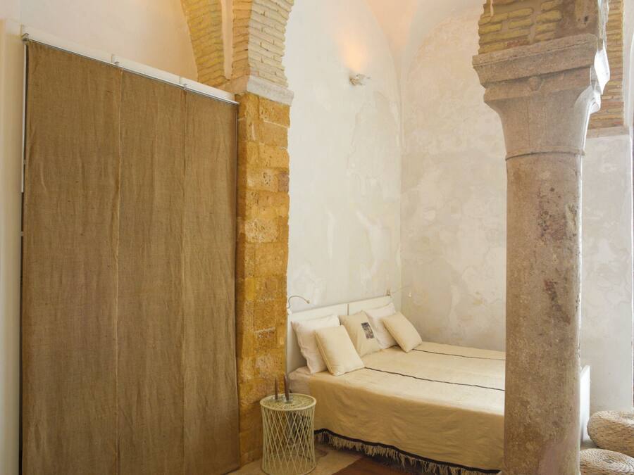 A room with a bed, a wooden wardrobe, a stone pillar, and a small round table.
