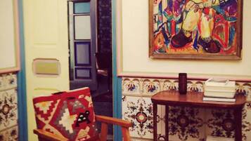 Una habitación con pared estampada, una silla de madera, una mesa con libros y un cuadro colorido.