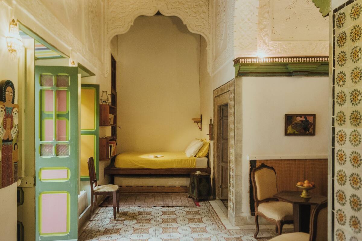 A traditional room with a bed, a chair, a small table, and a decorative wall.