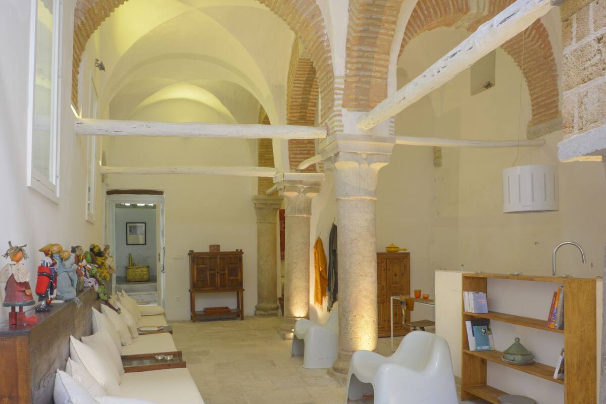A spacious interior with high ceilings and arched brick columns, featuring a white sofa and a wooden bookshelf.