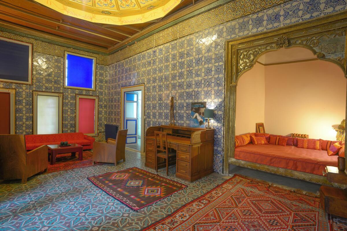 A room with patterned tile walls, a wooden desk, a red sofa, and a patterned rug.