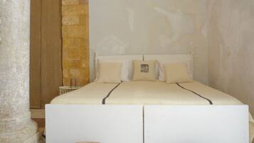 Un dormitorio con una cama grande, paredes de piedra y un taburete redondo tejido.