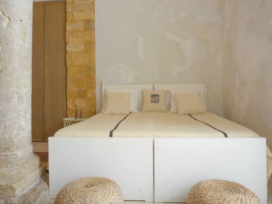 A bedroom with a large bed, stone walls, and a small round woven stool.