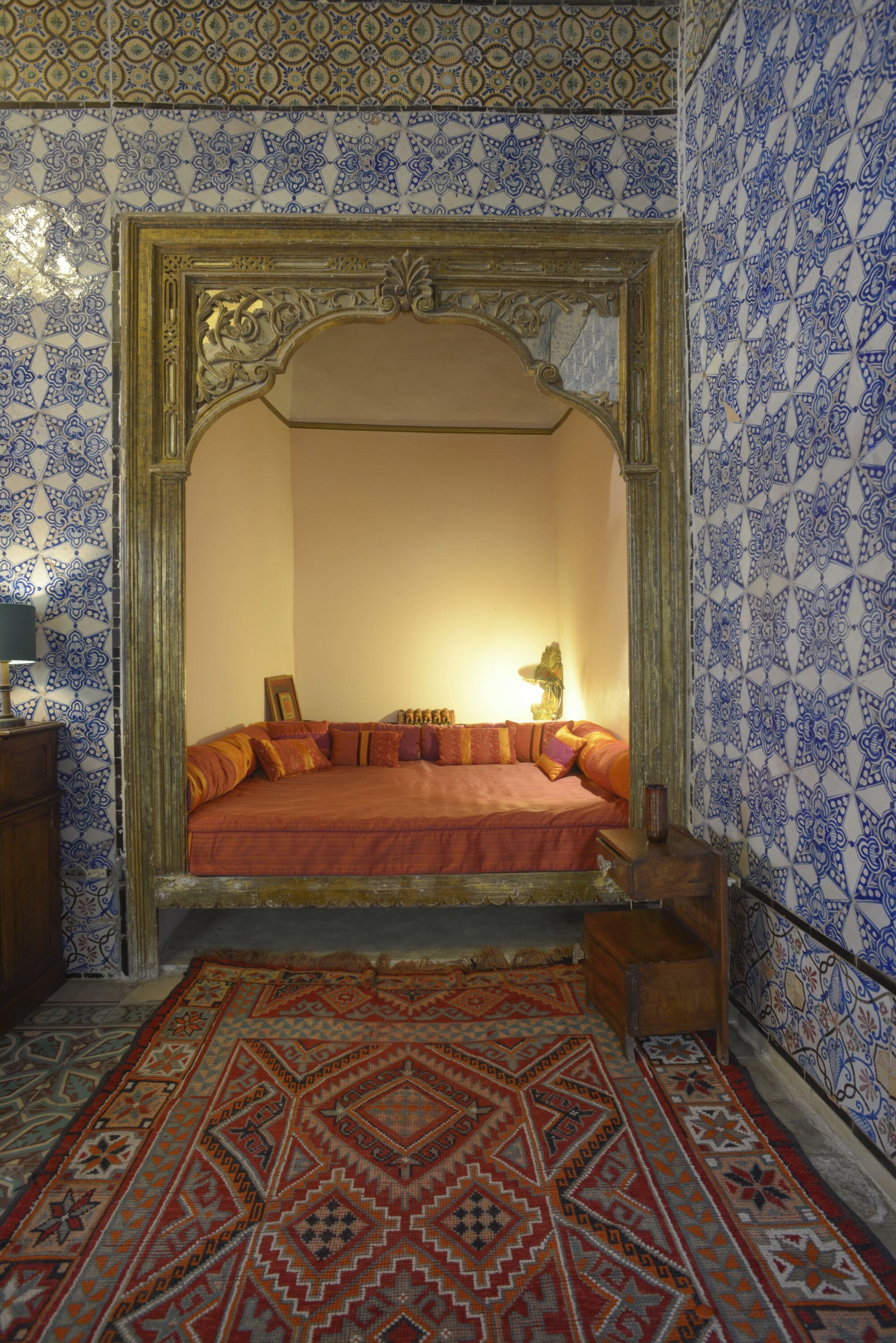 Een kamer met een bed, een kamerbreed tapijt en wanden met blauw-witte tegels.
