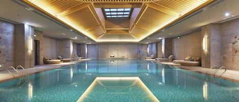 A large indoor swimming pool with a central diving platform, surrounded by lounge areas with seating.