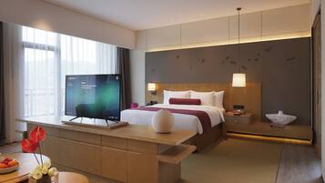 Een hotelkamer met een bed, nachtkastje, televisie, en een bureau met stoel en een vaas bloemen.