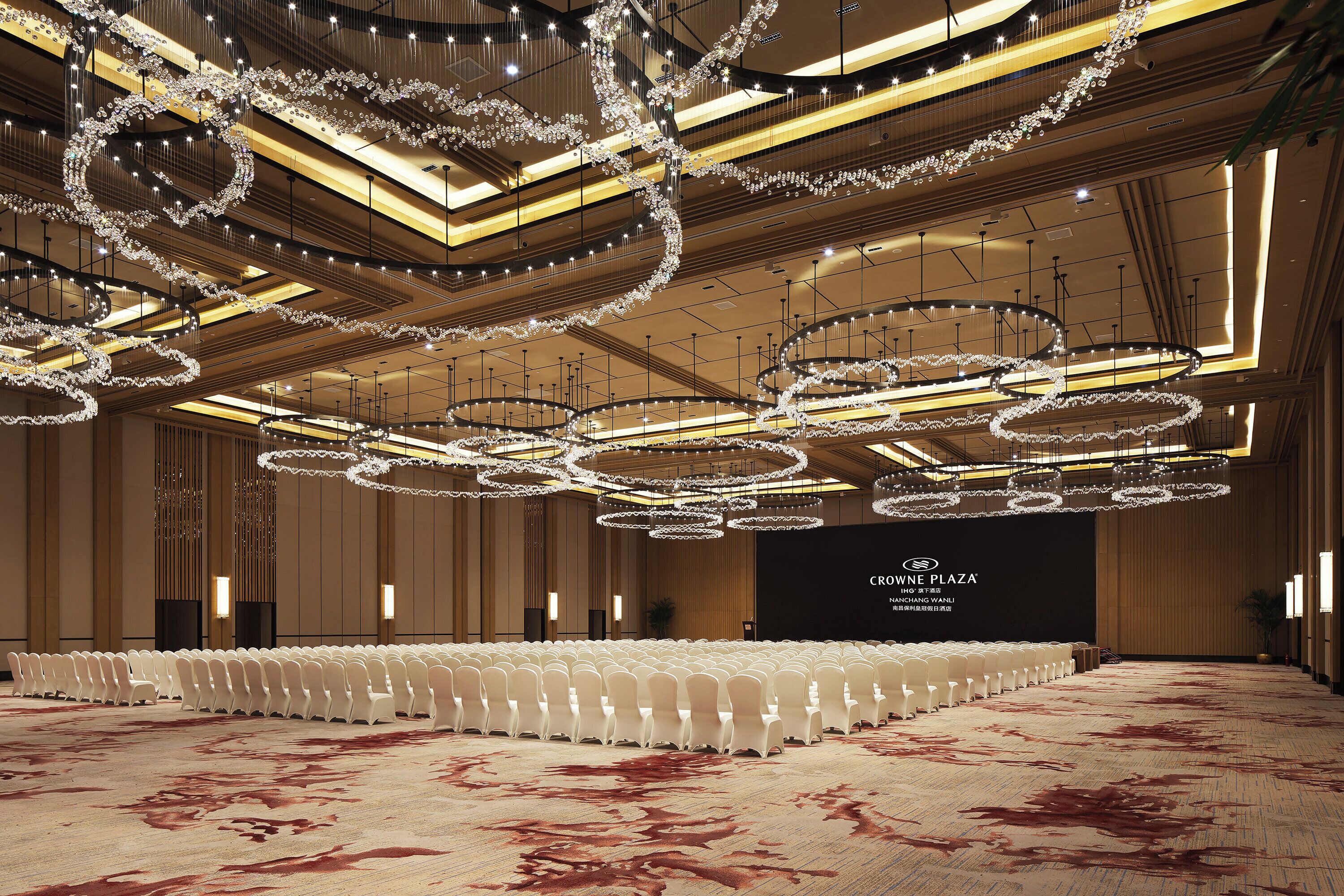 A spacious indoor venue with multiple tiers of seating, ornate chandeliers, and a large stage area.