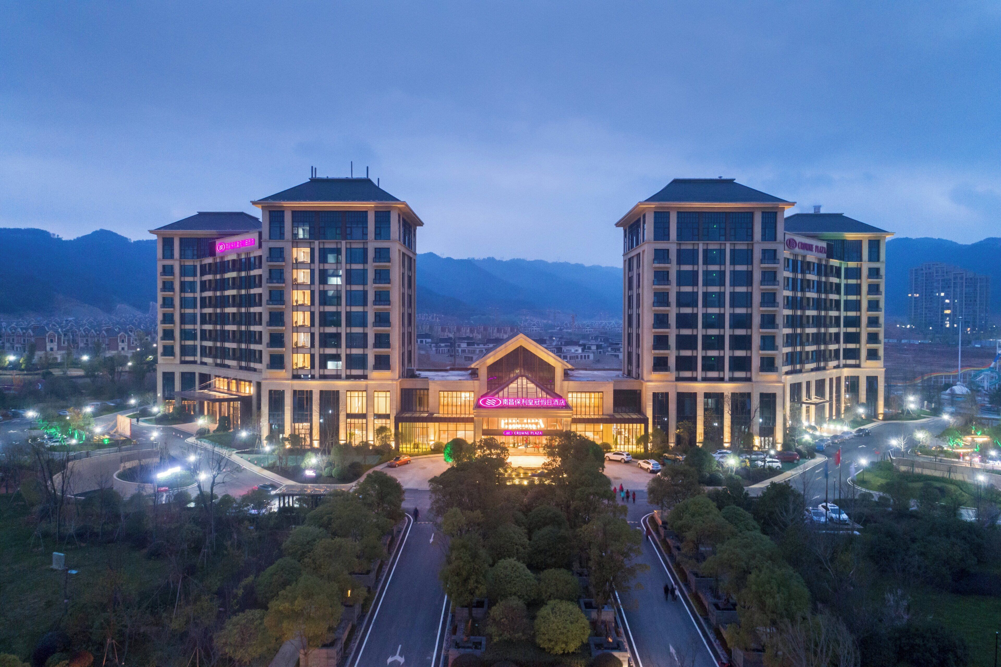 Un hotel con un edificio central y dos torres simétricas, rodeado de jardines cuidados y vistas a montañas distantes.