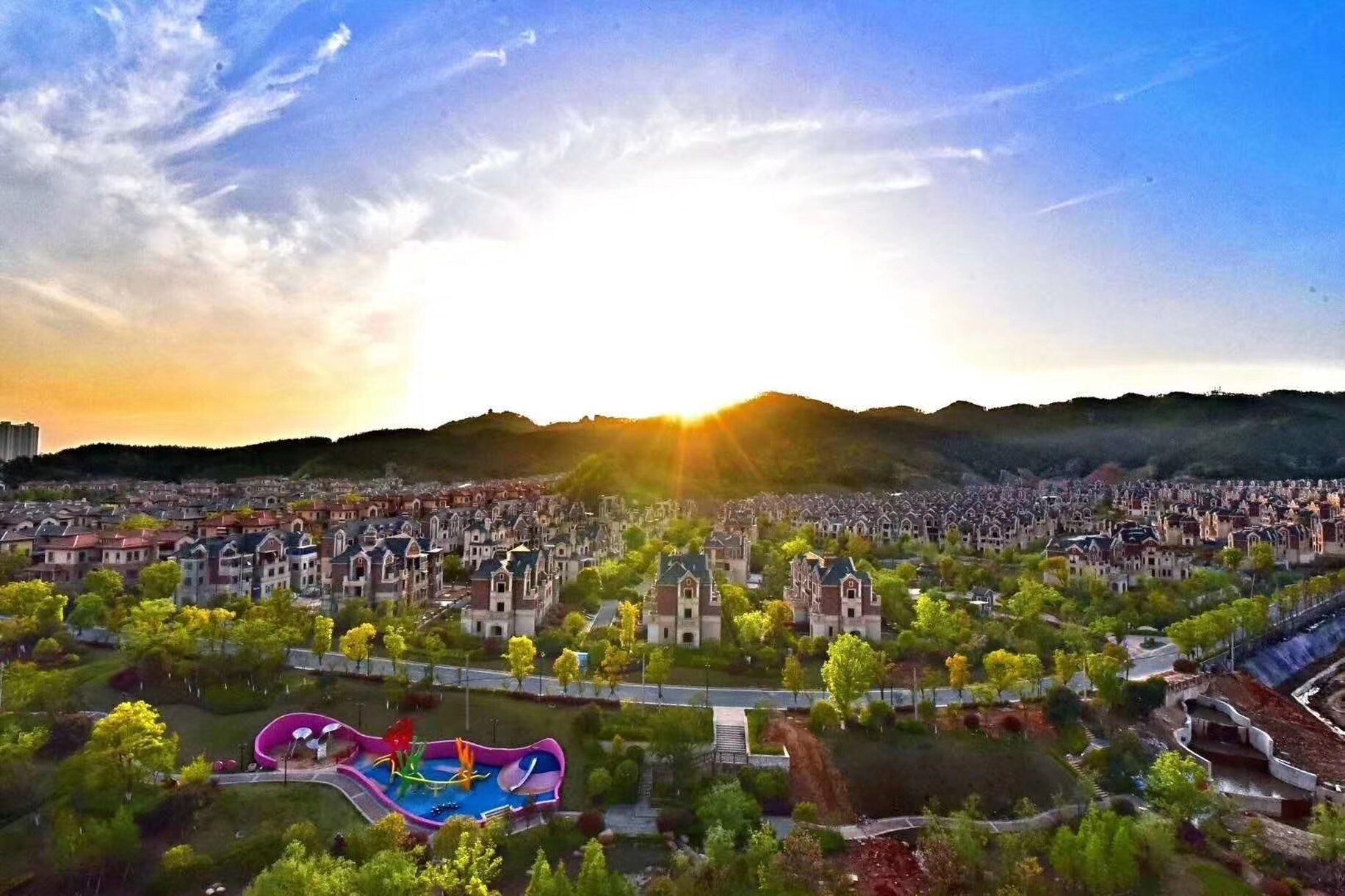 A residential area with a large park featuring a colorful playground and a water slide.