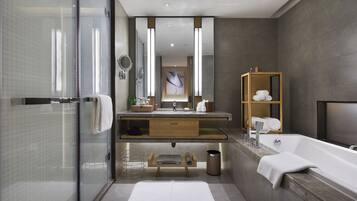 Un baño moderno con cabina de ducha de cristal, un espejo grande, tocador de madera, bañera y una toalla blanca en el suelo.