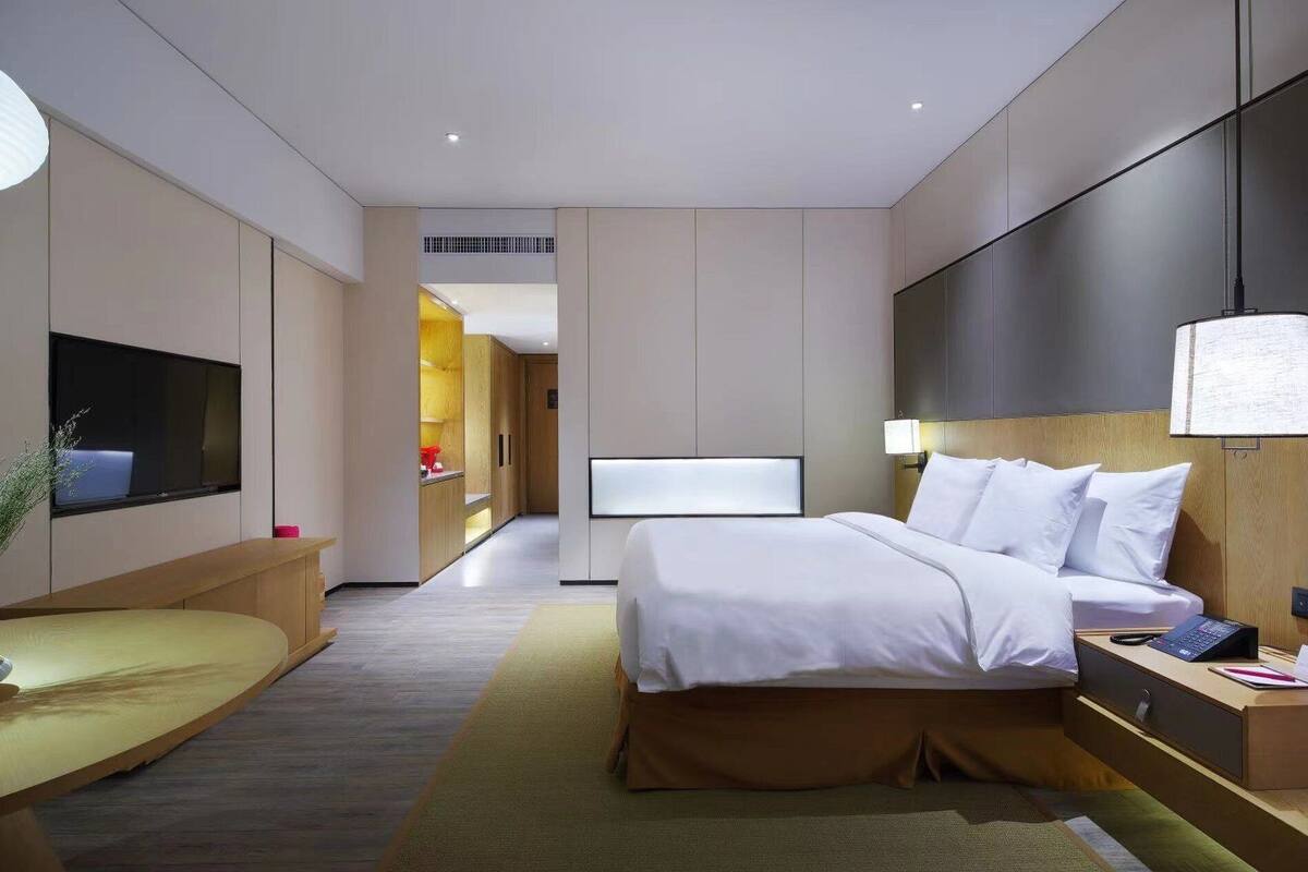 Una habitación de hotel moderna con una cama grande, mesitas de noche, un televisor y un escritorio con lámpara.