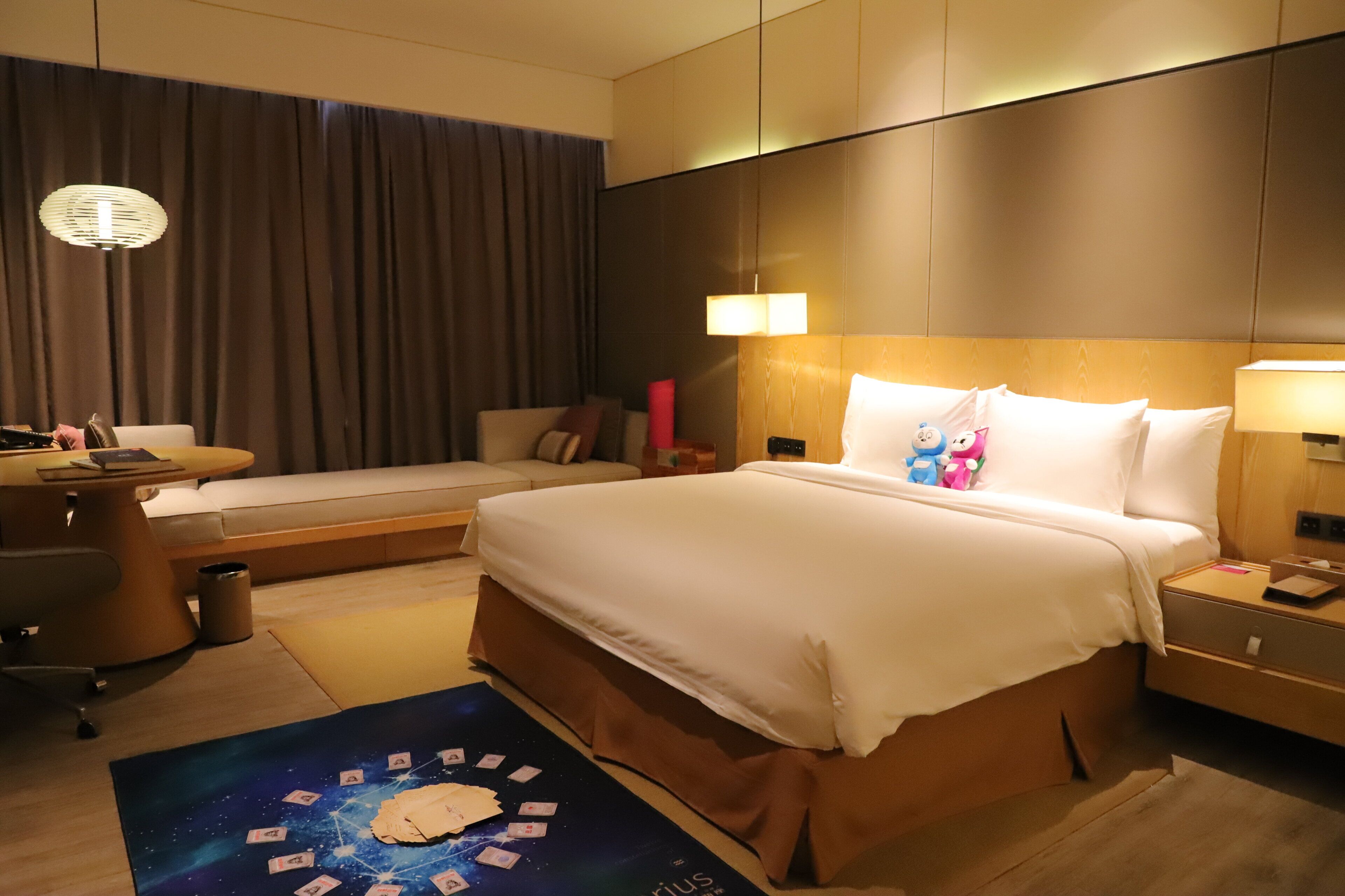 A hotel room with a bed, bedside tables, a desk, a chair, and a view of the outside.