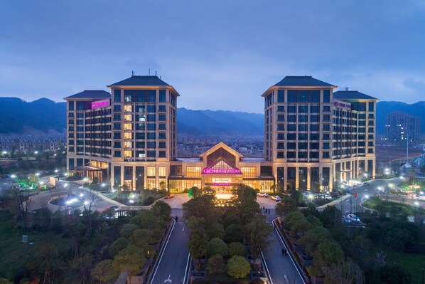 A hotel with a central building flanked by two towers, surrounded by greenery and a mountainous backdrop. - Crowne Plaza Nanchang Wanli by IHG (Nanchang)