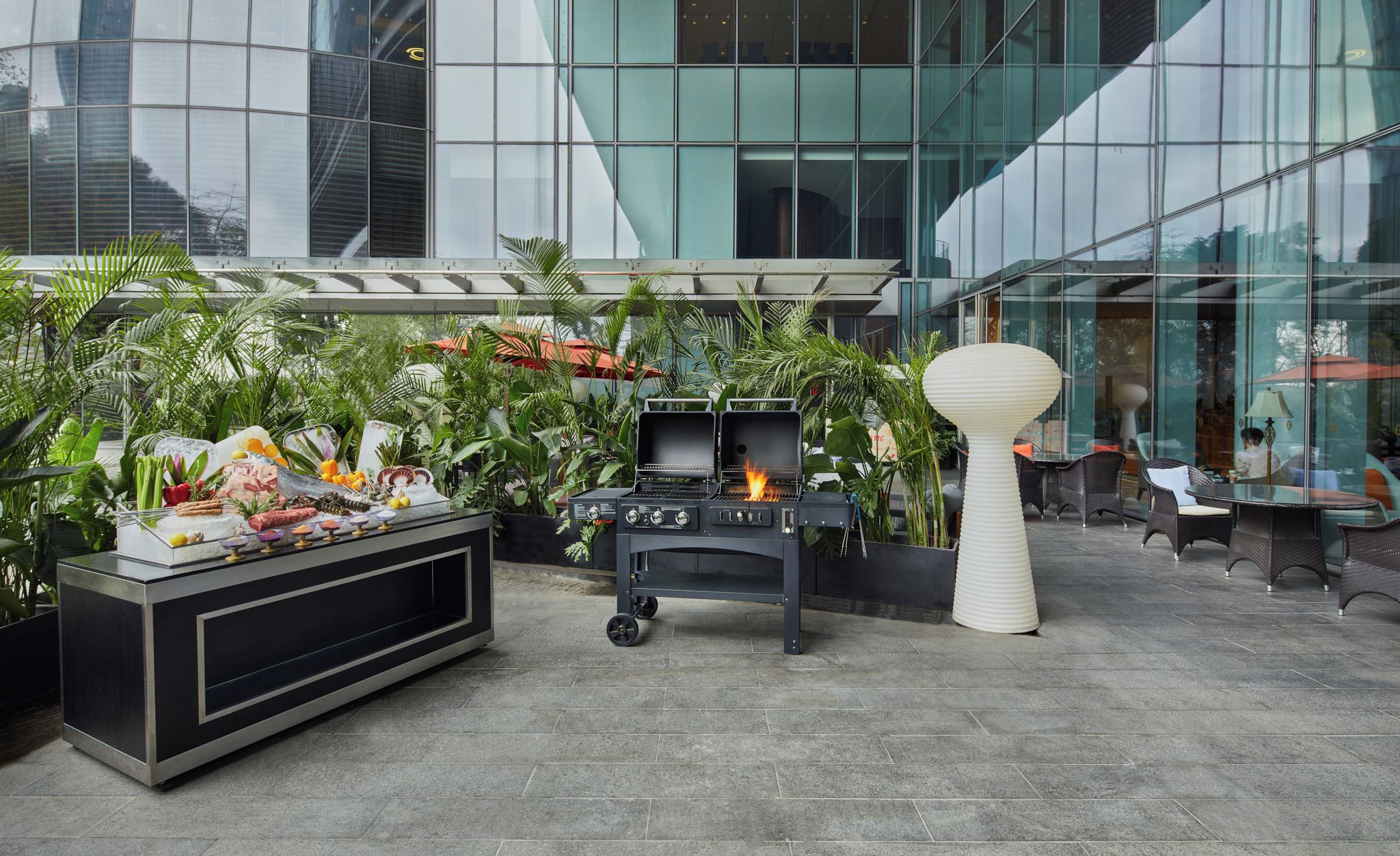 An outdoor patio with a grill, a buffet table with food, and potted plants.