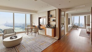 Amplia habitación de hotel con un gran ventanal que ofrece vistas a la ciudad, una cocina moderna y una zona de estar confortable con una mesa de centro redonda.