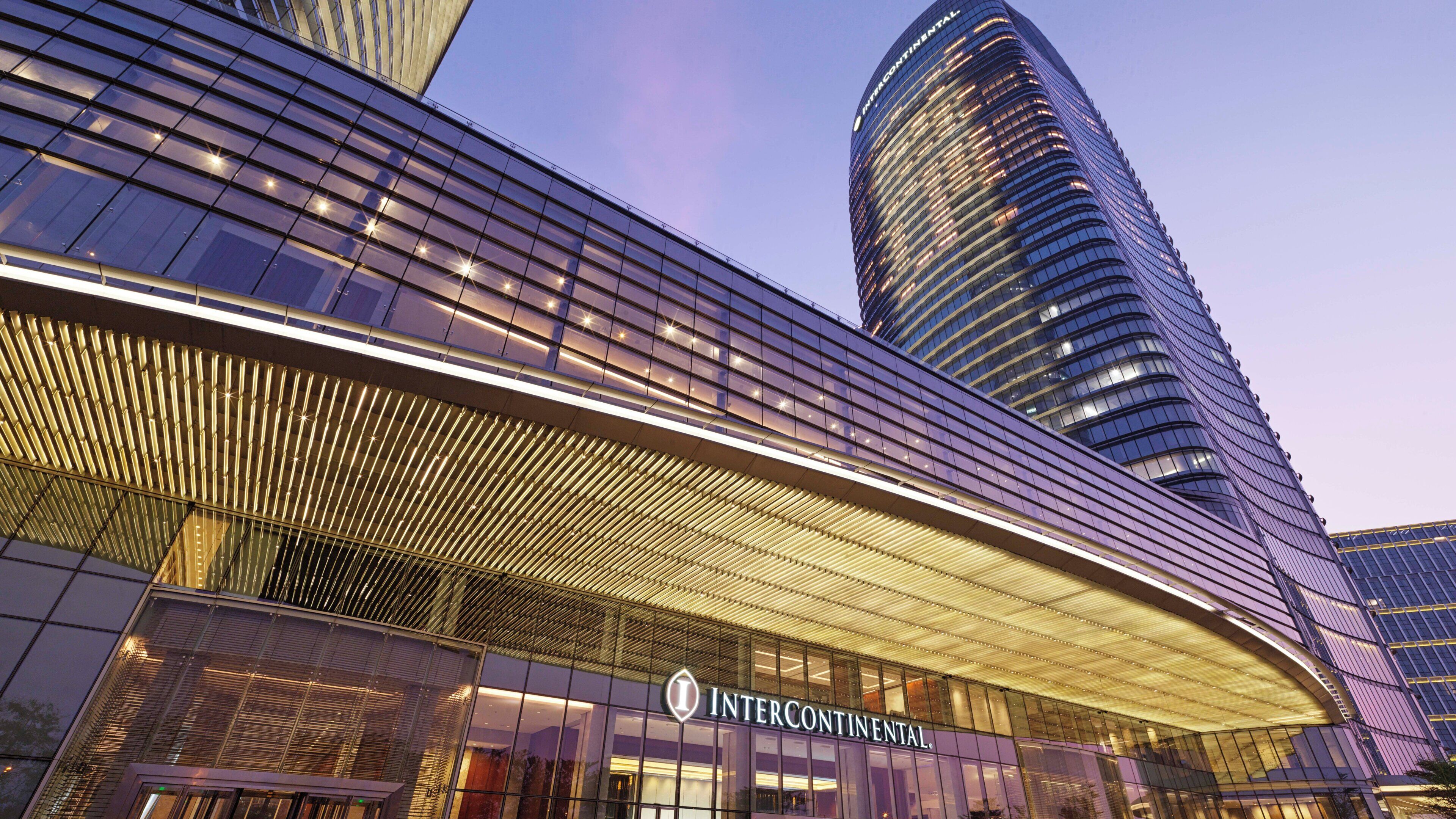 A modern hotel with a prominent curved glass facade and a distinctive overhanging structure.