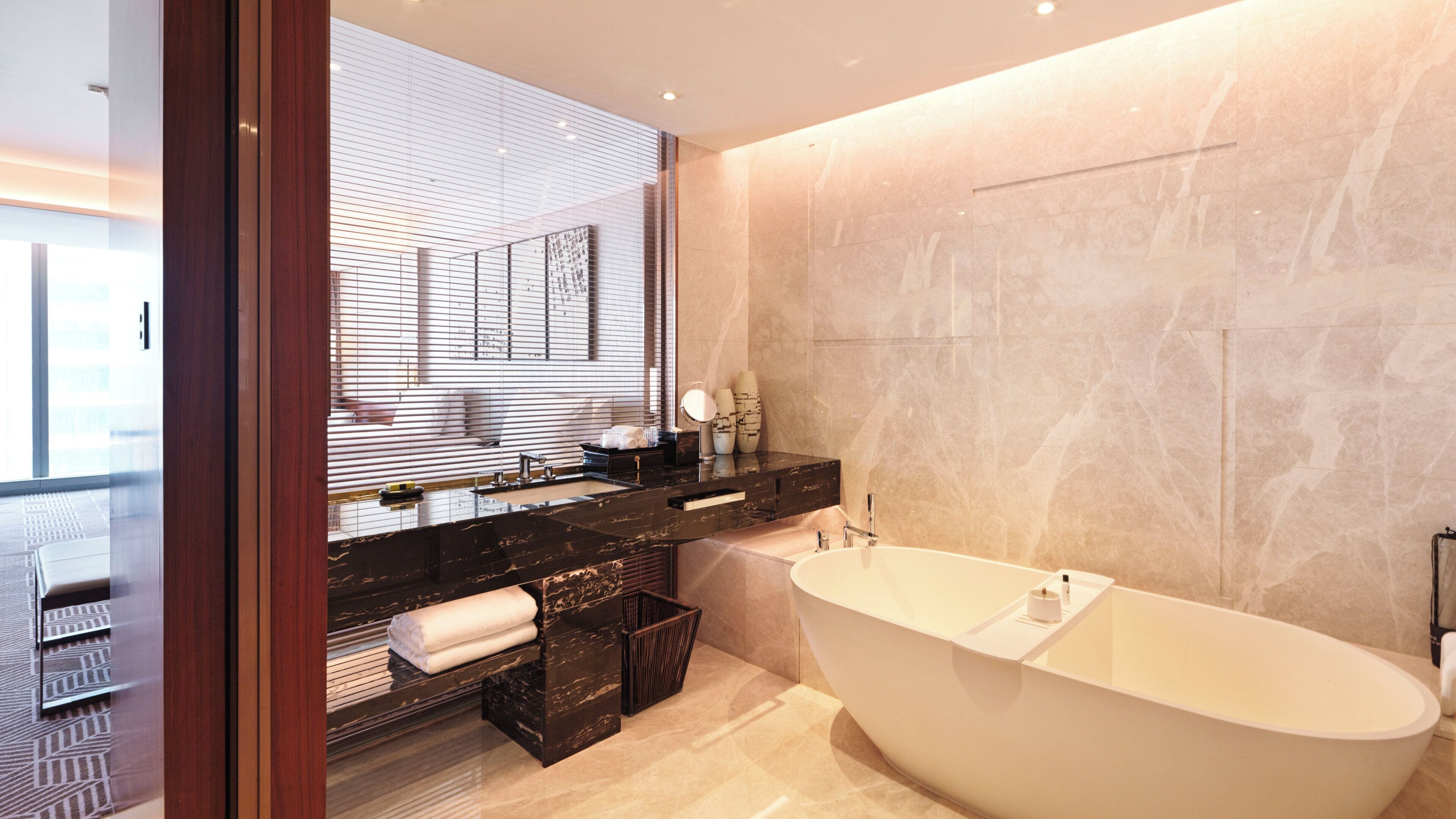 A modern bathroom with a freestanding bathtub, a large mirror, and a vanity with a black marble countertop.
