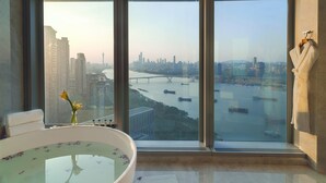 Un baño moderno con una bañera grande, vistas de un paisaje urbano y una ventana con una bata colgada en el alféizar.