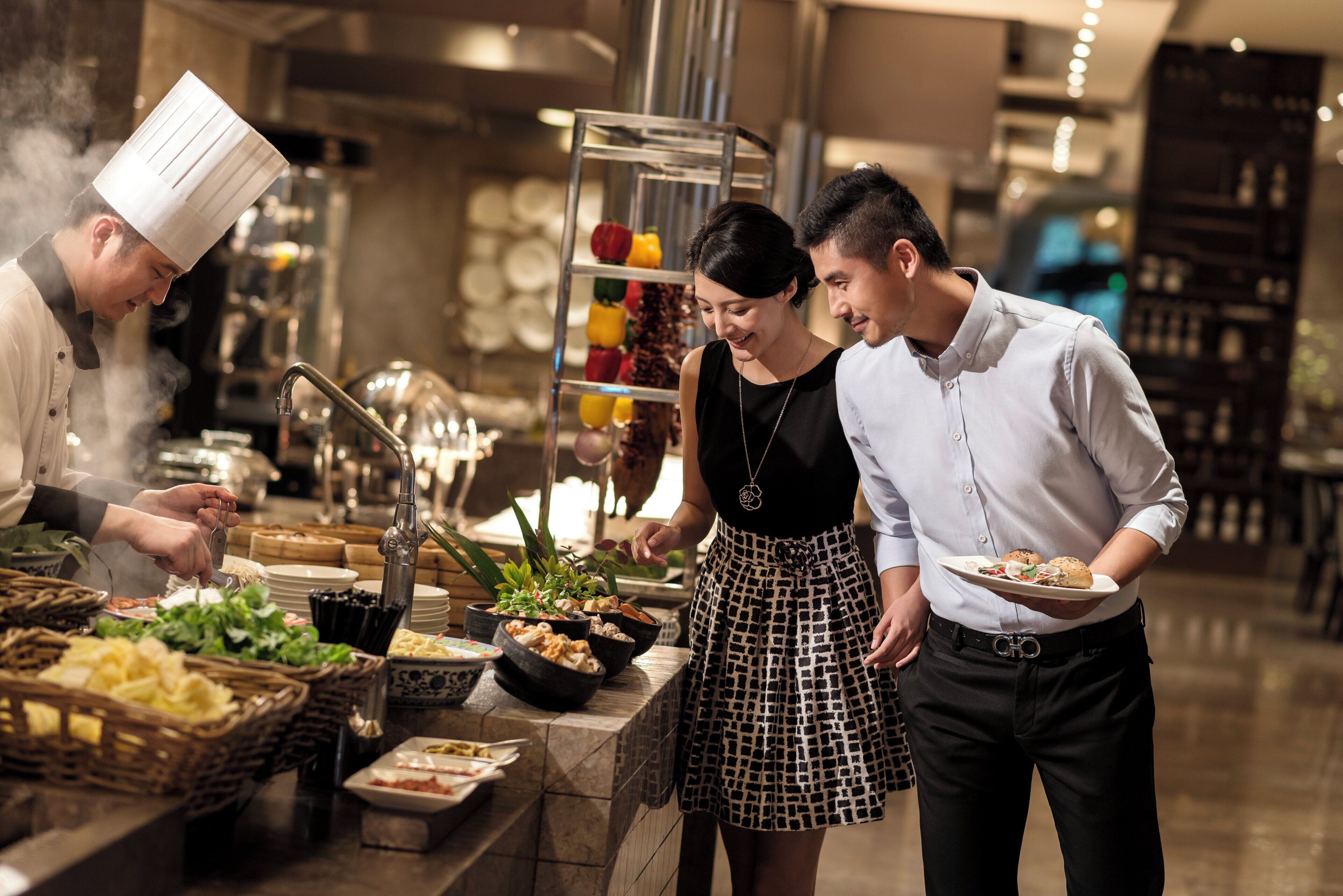 A buffet setup with various food items and a chef preparing food.