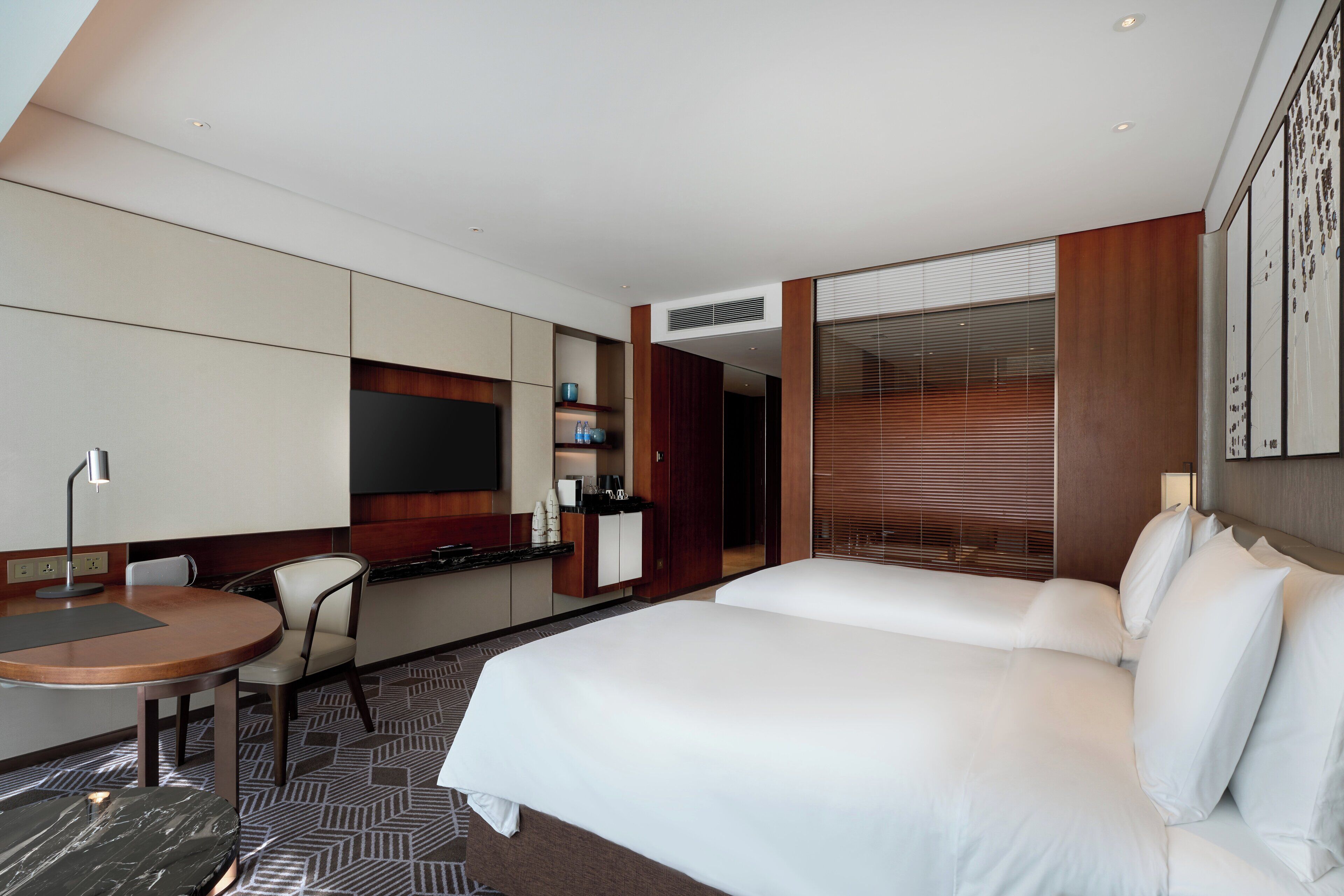 A hotel room with a bed, a desk, a chair, a TV, and a minibar.